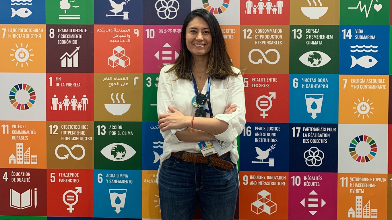 Alejandra standing in front of the icons for the 17 Sustainable Development Goals